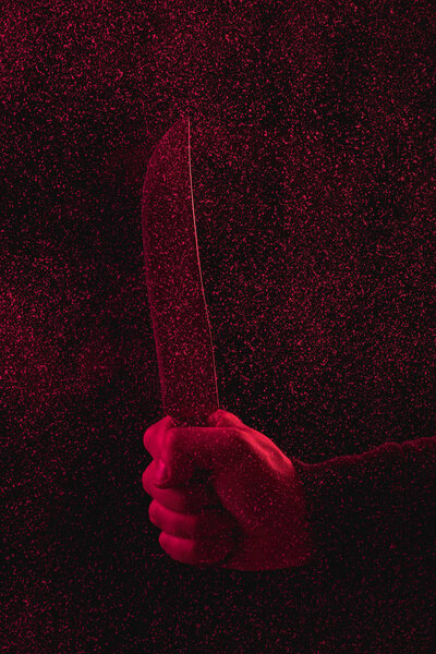 cropped shot of man holding knife in red light 