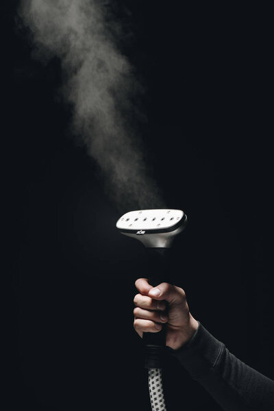 close-up partial view of person holding garment steamer with steam on black