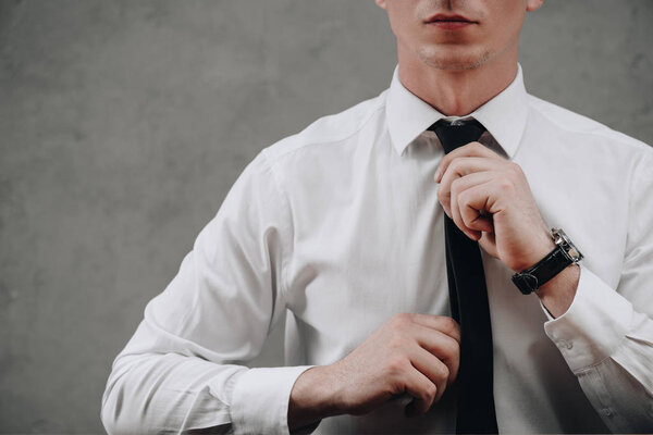 cropped shot of businessman adjusting necktie on grey