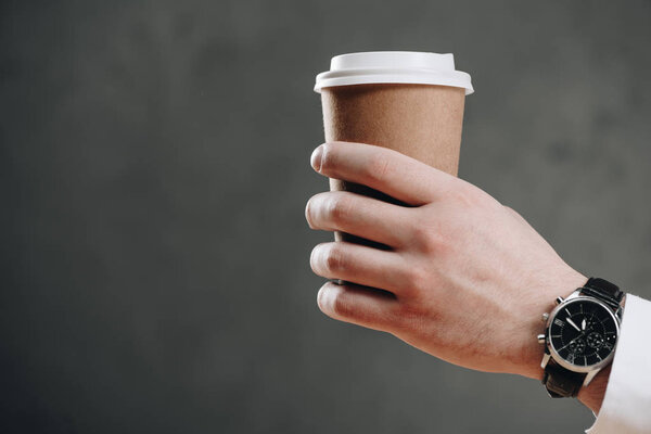 cropped shot of businessman holding paper cup with coffee to go on grey