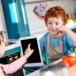デジタル タブレットを使用して、一緒にキッチンで料理をしながら子供たちがかわいい