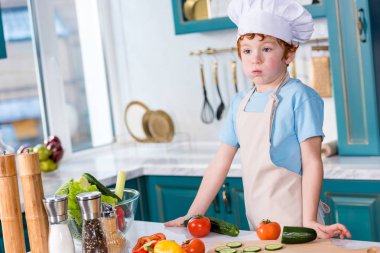sevimli küçük çocuk chef şapka ve uzak mutfakta yemek yaparken seyir önlük