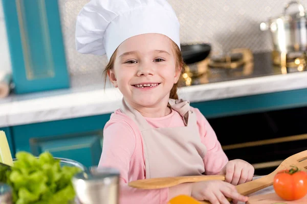 Bedårende Barn Kok Hat Forklæde Smilende Kameraet Mens Madlavning Køkkenet - Stock-foto
