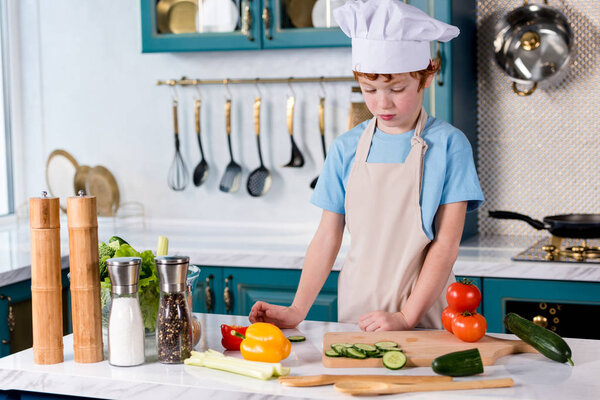 cute little boy in chef hat and apron cooking in kitchen