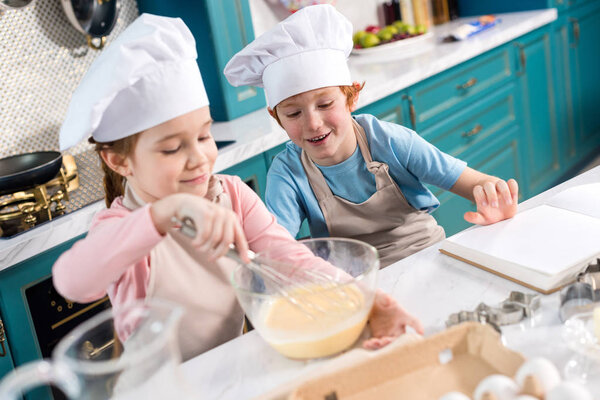 happy children in chef hats making tough in kitchen
