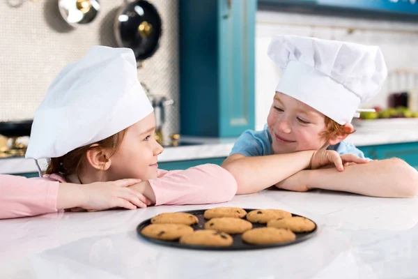 Gelukkige Kinderen Chef Kok Hoeden Glimlachen Elkaar Heerlijke Koekjes Tafel — Gratis stockfoto