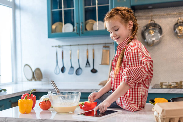 cute smiling child using digital tablet while cooking in kitchen