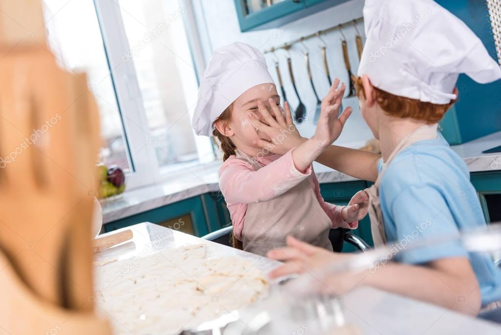selective focus of adorable little children in chef hats having fun with flour in kitchen