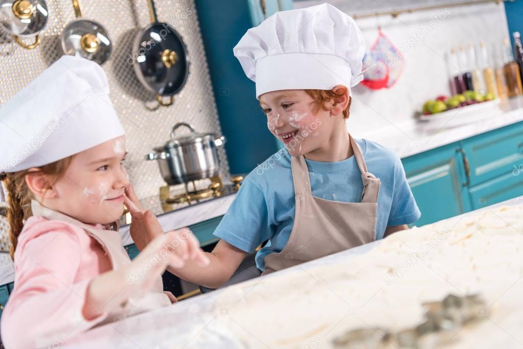 cute little kids in chef hats having fun with flour in kitchen