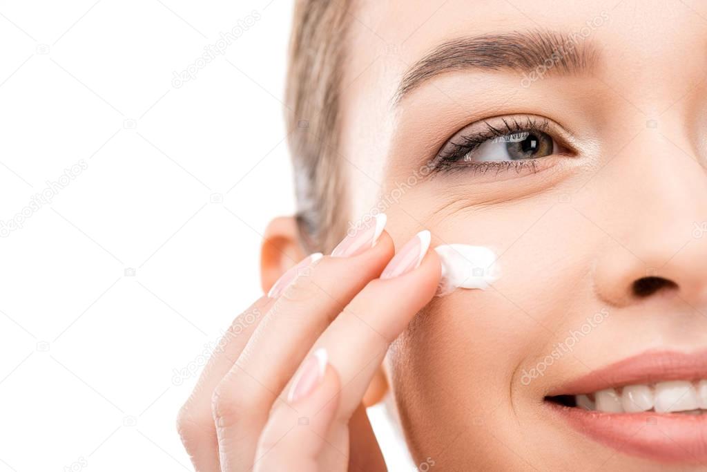 cropped view of young woman applying cosmetic cream, isolated on white