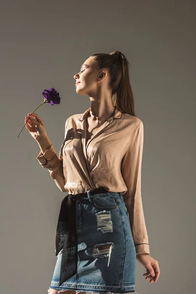 beautiful girl in denim skirt and blouse holding flower, isolated on grey