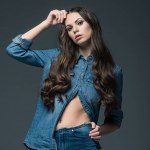 Krásná elegantní dívka s dlouhými vlasy pózuje v džínách, izolované Grey