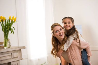 beautiful happy mother and daughter piggybacking and smiling at camera clipart