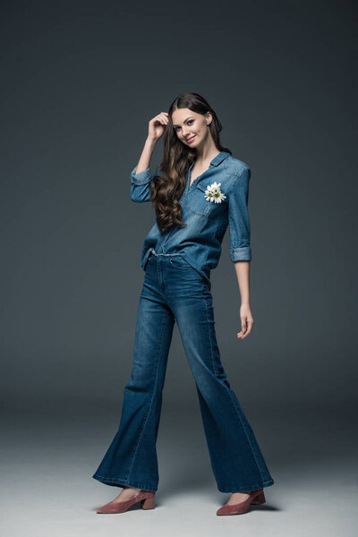 beautiful smiling girl with long hair posing in flare jeans, on grey