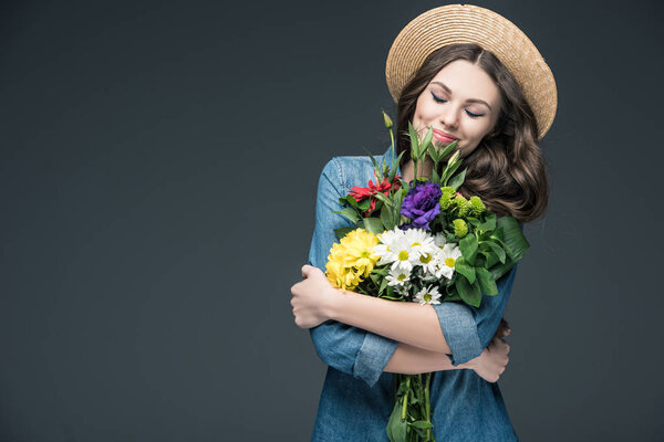 красивая счастливая женщина с закрытыми глазами, держащая цветы на 8 марта, изолированная на сером
