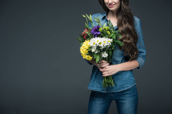 cropped view of girl in denim clothes holding bouquet of flowers for international womens day, isolated on grey