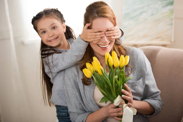 Fröhliches Kind Schließt Augen Vor Fröhlicher Mutter Mit Gelben Tulpen — Stockfoto