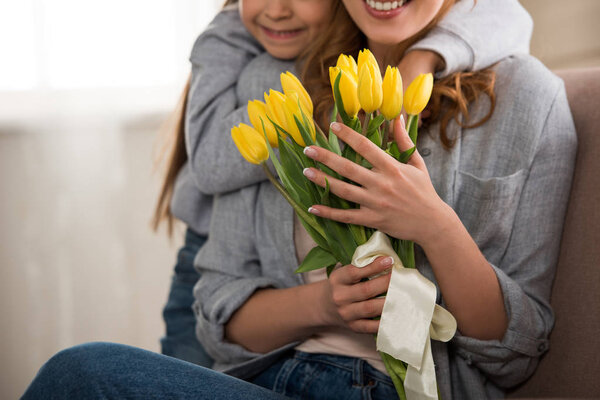 cropped shot of happy child hugging smiling mother with yellow tulips