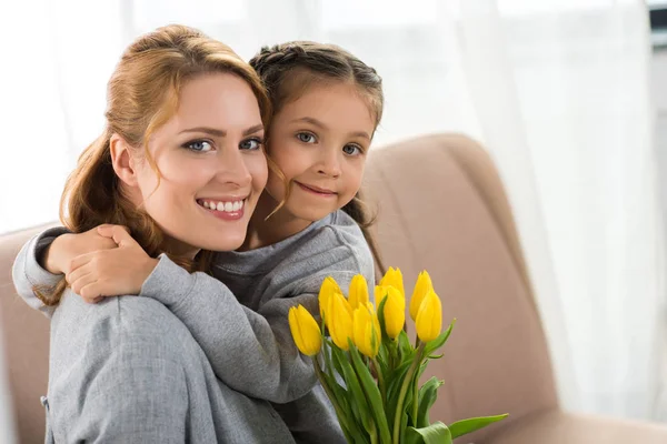 愉快的母亲和女儿与黄色郁金香拥抱和微笑在照相机 — 图库照片