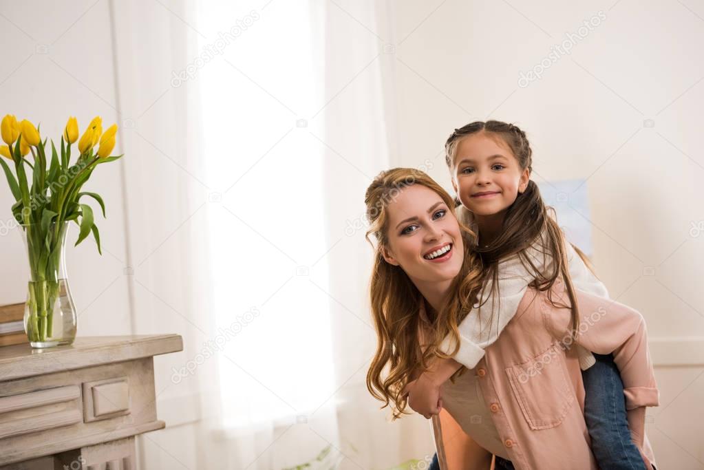 beautiful happy mother and daughter piggybacking and smiling at camera