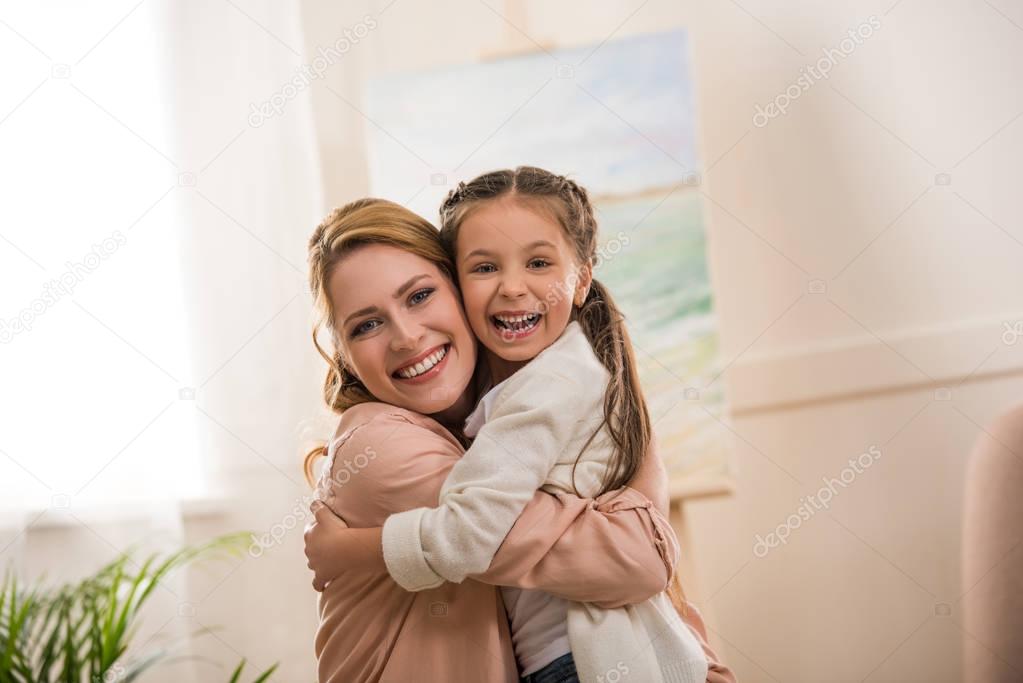 happy mother and daughter hugging and smiling at camera at home