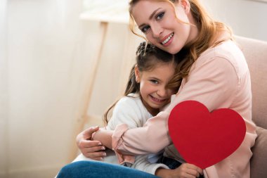 mutlu anne ve kızı kırmızı kalp ile sarılma ve kameraya gülümseyen simgesi