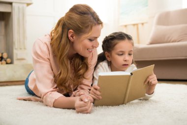 mutlu anne ve kızı halı üzerinde yalan ve birlikte kitap okuma