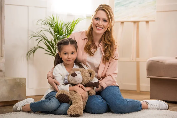 Feliz Madre Hija Pequeña Con Osito Peluche Sentado Juntos Sonriendo —  Fotos de Stock