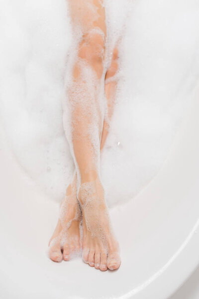 partial view of female legs in bath with foam
