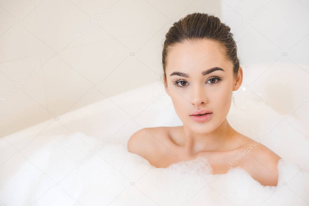 portrait of attractive young woman taking bath with foam at home