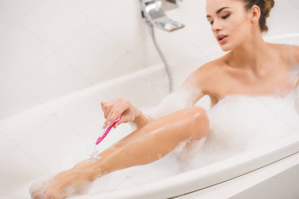 young woman shaving legs while taking bath at home