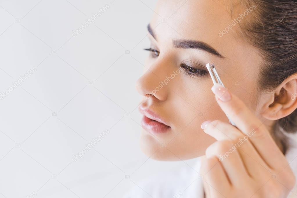 young woman plucking eyebrows with tweezers