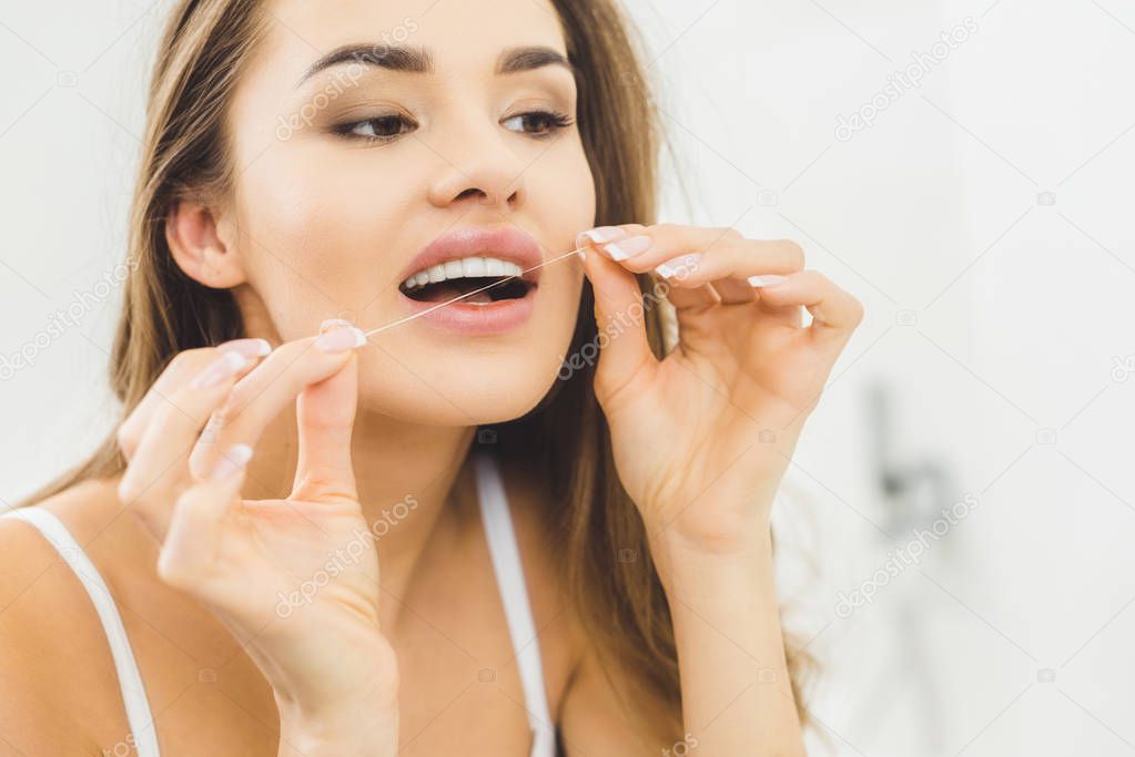 portrait of beautiful woman cleaning teeth with dental floss