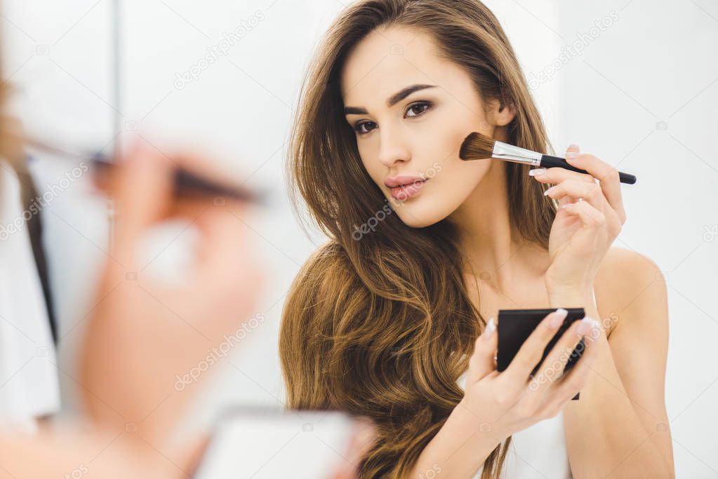 mirror reflection of beautiful young woman applying makeup