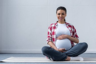 Yoga mat üzerinde oturan Afro-Amerikan hamile kadın