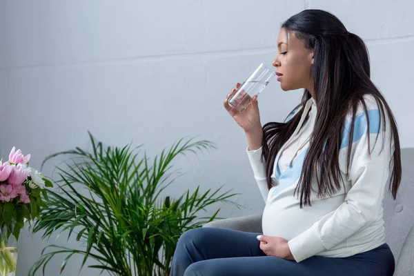 African American Pregnant Woman Drinking Water While Sitting Armchair — Stock Photo, Image