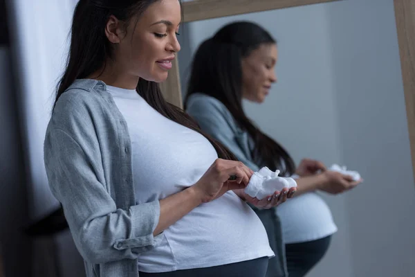 African American Pregnant Woman Holding Little Socks Standing Mirror — Stock Photo, Image
