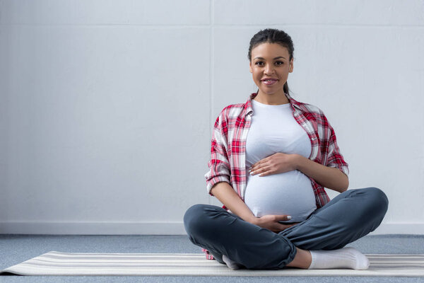 african american pregnant woman sitting on yoga mat