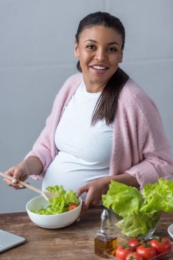 gülümseyen Afro-Amerikan hamile kadın mutfak at salatası yapmak