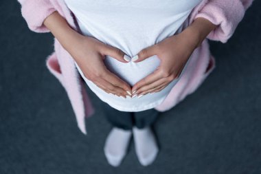 cropped view of pregnant girl making heart symbol with hands on her belly clipart