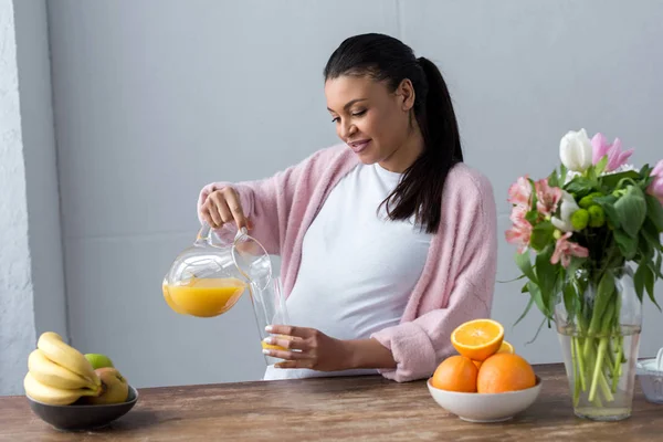 キッチンで新鮮なフルーツ ジュースを注いで妊娠中のアフリカ系アメリカ人の女性 — ストック写真