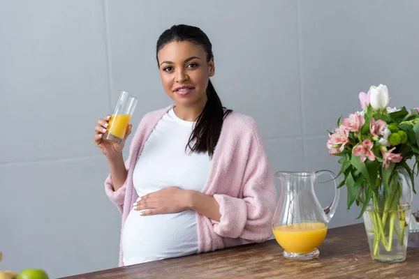キッチンでのオレンジ ジュースのガラスとアフリカ系アメリカ人の妊娠中の女性 — ストック写真