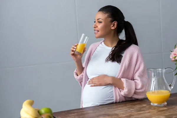 キッチンでのオレンジ ジュースのガラスとアフリカ系アメリカ人の妊娠中の女性 — ストック写真