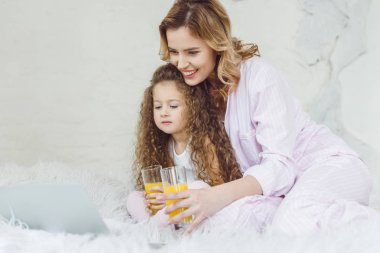 Anne ve portakal suyu yatakta dizüstü kullanarak gözlüklü kıvırcık kız
