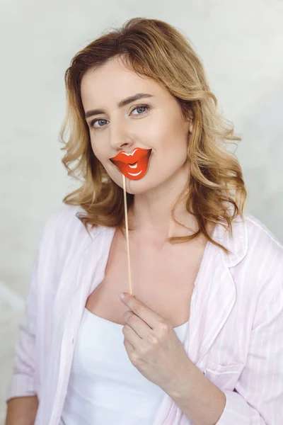 blonde woman in pajamas holding red paper lips on stick