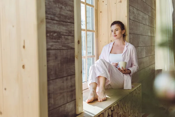 Düşünceli Kadın Kahve Tutarak Pencere Kenarında Oturan Pijama — Stok fotoğraf