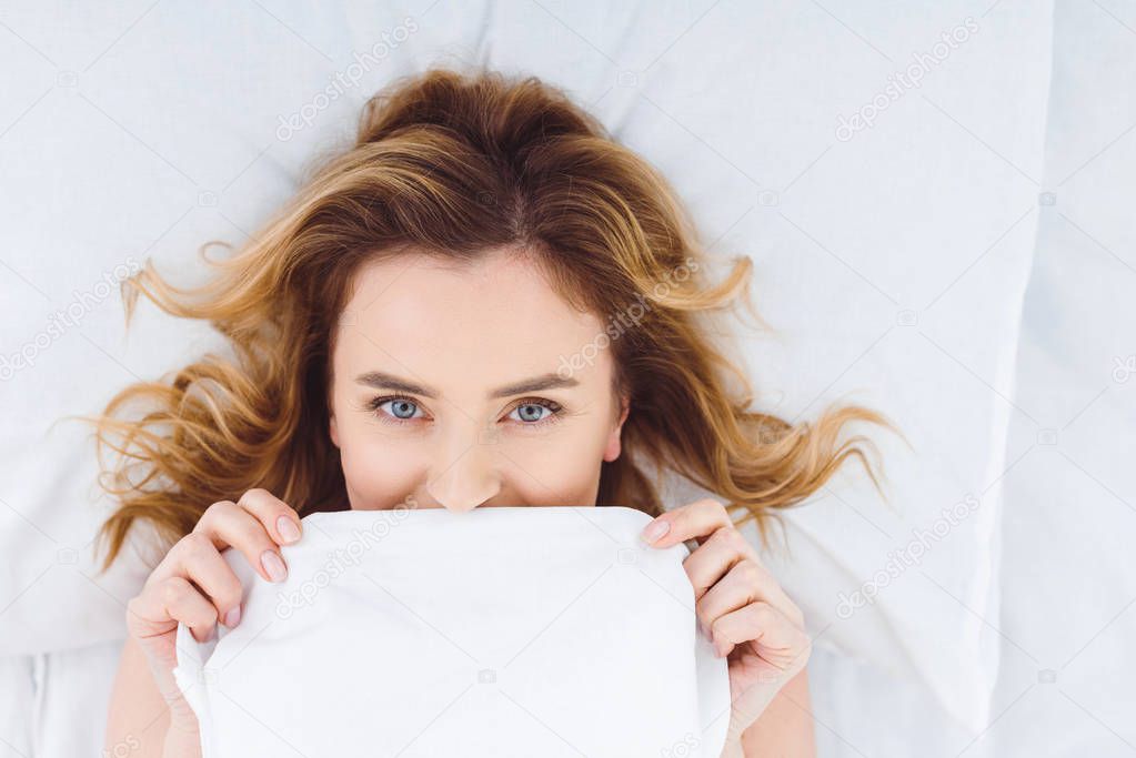 top view of happy woman lying in bed and covering with blanket