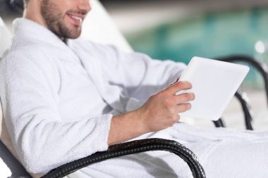 spa Center'da dijital tablet kullanarak bornoz erkekte gülümseyen in atış kırpılmış