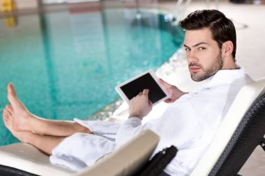Dijital tablet kullanma ve spa merkezi kamerada bakarak bornoz yakışıklı adam