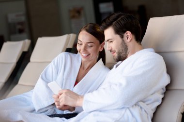 spa merkezinde dinlenme sırasında birlikte smartphone kullanarak bornoz mutlu genç Çift